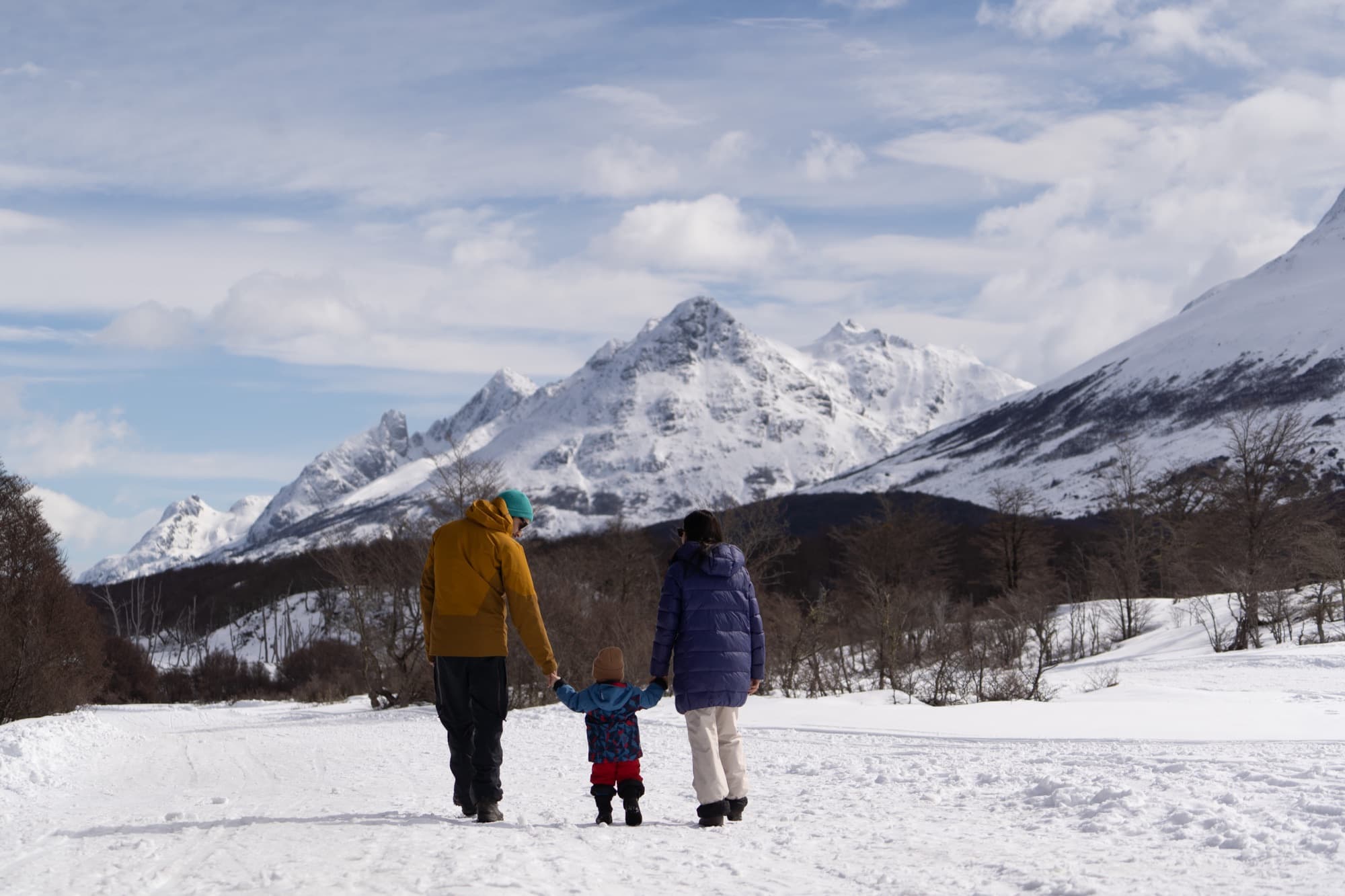 Familia caminando en la nieve entre montañas
